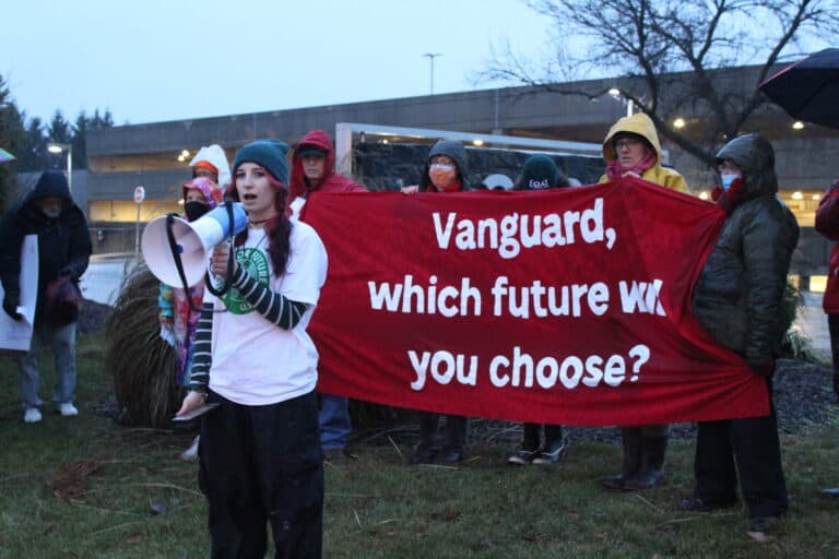 A young person speaks into a megaphone, in front of other activists holding a banner that reads "Vanguard, which future will you choose?)