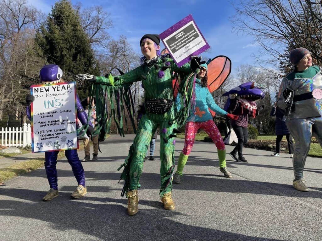 A half dozen people in colorful animal costumers dance in the middle of a street. Some are holding signs, including one that says "New year, new Vanguard?? Ins: - take climate change seriously, -make climate-safe investments the default, - vote for climate-friendly shareholder resolutions"