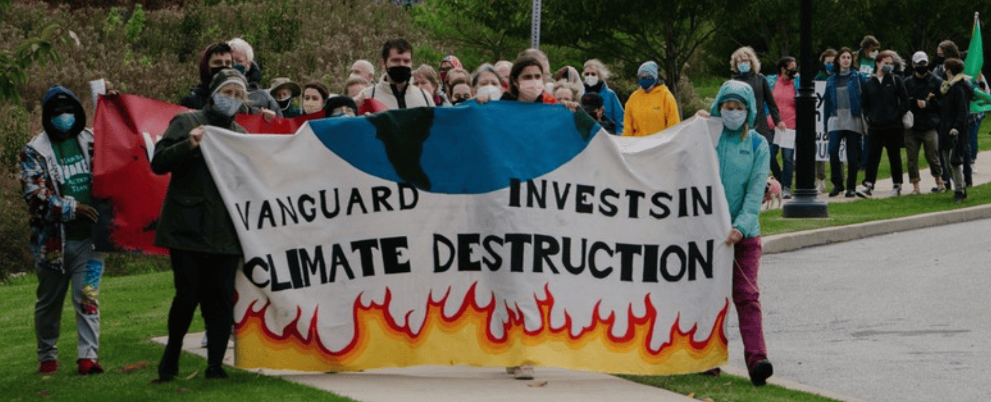 Group of people walk behind a banner that reads, "Vanguard invests in climate destruction"