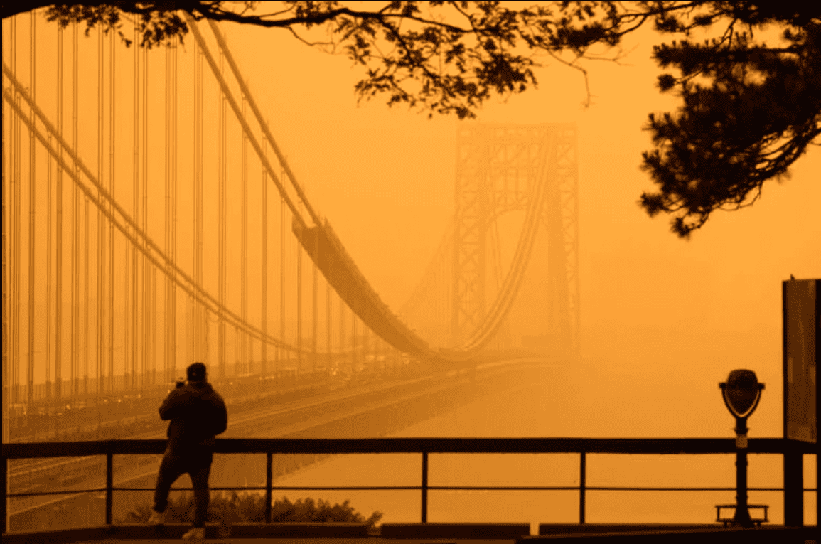 Silhouetted against orange, hazy air, a person stands and looks towards a bridge