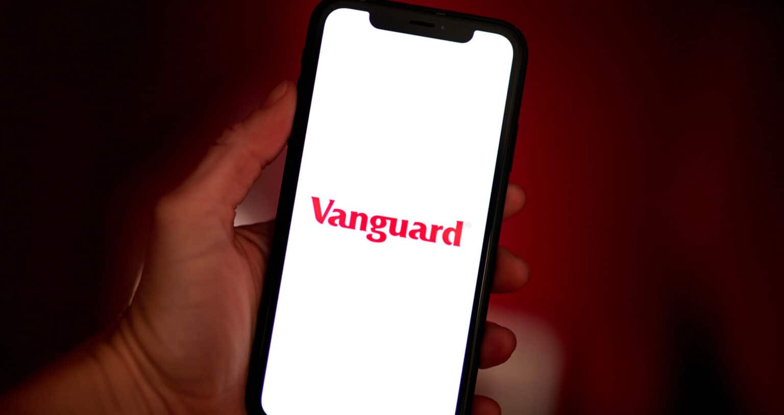 A hand holds a smartphone with a bright white screen with the red Vanguard logo in the middle